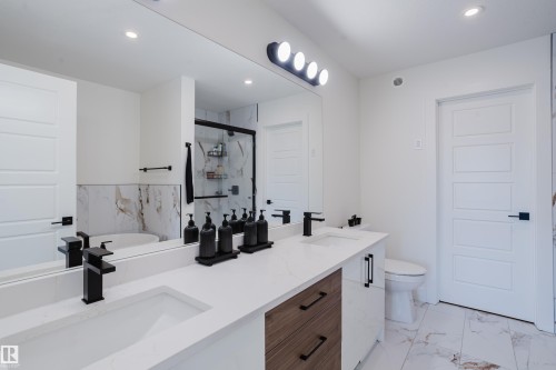 Bathroom featuring a dual vanity with white countertops, modern black faucets, and a combination of white and wood-toned cabinetry - 79 Silverstone Drive, Stony Plain, AB - Indoor Photo Showing Bathroom
