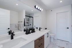 Bathroom featuring a dual vanity with white countertops, modern black faucets, and a combination of white and wood-toned cabinetry - 