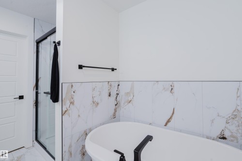 Bathroom featuring a freestanding bathtub with matte black fixtures, a shower enclosure with a clear glass door and black frame, and wall tiling with a marble-effect pattern - 79 Silverstone Drive, Stony Plain, AB - Indoor Photo Showing Bathroom