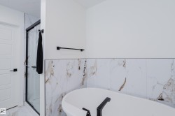 Bathroom featuring a freestanding bathtub with matte black fixtures, a shower enclosure with a clear glass door and black frame, and wall tiling with a marble-effect pattern - 