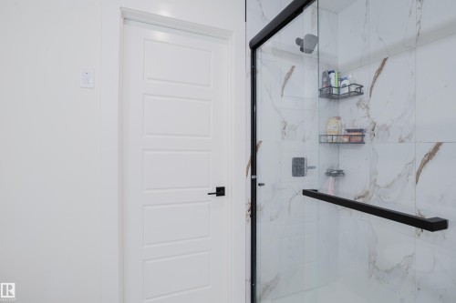 Contemporary shower enclosure featuring clear glass and matte black framing, complemented by white and brown marbled wall tiles - 79 Silverstone Drive, Stony Plain, AB - Indoor Photo Showing Bathroom
