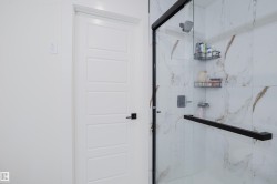 Contemporary shower enclosure featuring clear glass and matte black framing, complemented by white and brown marbled wall tiles - 