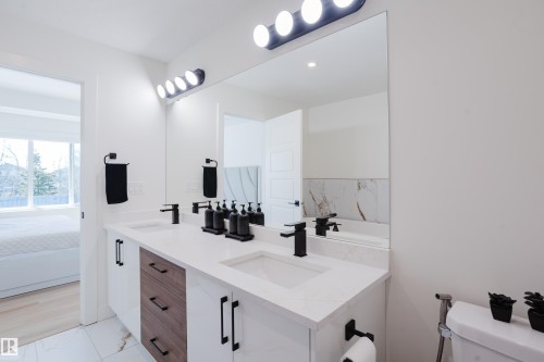 Bathroom featuring a large double vanity with white countertops, integrated sinks, dark wood and white cabinetry, and matte black hardware - 79 Silverstone Drive, Stony Plain, AB - Indoor Photo Showing Bathroom