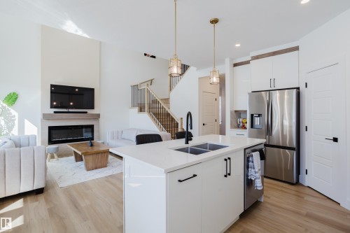 Open concept living area featuring a kitchen island with a double sink, a stainless steel refrigerator, and light wood flooring - 79 Silverstone Drive, Stony Plain, AB - Indoor Photo Showing Kitchen With Fireplace With Double Sink With Upgraded Kitchen