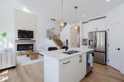 Open concept living area featuring a kitchen island with a double sink, a stainless steel refrigerator, and light wood flooring - 