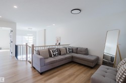 The property features light wood flooring, white walls, and a staircase with a black and light wood railing - 