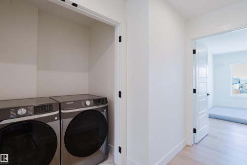 Laundry area featuring a side-by-side washer and dryer set, with a hallway and doorway leading to a room with light-colored flooring and a window - 79 Silverstone Drive, Stony Plain, AB - Indoor Photo Showing Laundry Room