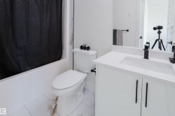 Bathroom featuring a white vanity with a rectangular sink, a toilet, a bathtub, and white tiled flooring - 
