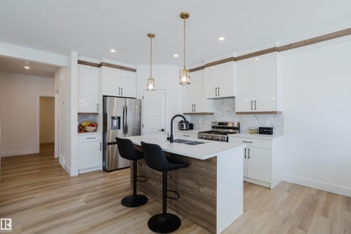 The kitchen features a central island with a countertop, sleek white cabinetry, and a stainless steel refrigerator and range - 79 Silverstone Drive, Stony Plain, AB - Indoor Photo Showing Kitchen With Upgraded Kitchen