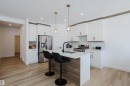 The kitchen features a central island with a countertop, sleek white cabinetry, and a stainless steel refrigerator and range - 79 Silverstone Drive, Stony Plain, AB  - Indoor Photo Showing Kitchen With Upgraded Kitchen 