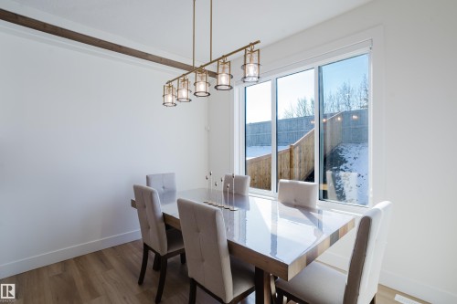The dining area features a modern linear chandelier and light wood-look flooring - 79 Silverstone Drive, Stony Plain, AB - Indoor Photo Showing Dining Room