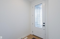 Entryway featuring a white door with decorative glass inserts, matte black hardware, and light-toned flooring - 