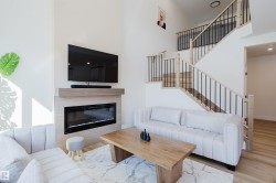 The living area features an electric fireplace with a wood-toned mantel, a light-toned staircase with black metal balusters, and light-colored flooring - 