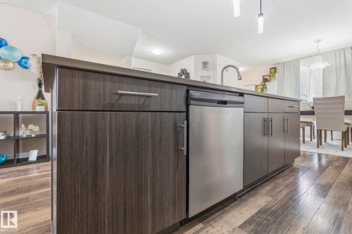 The property features an island with dark wood cabinetry and a stainless steel dishwasher - 4783 Crabapplle Run, Edmonton, AB - Indoor Photo Showing Other Room