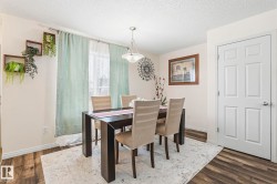 This dining area features wood-look flooring, light-colored walls, and a window with sheer and patterned curtains - 