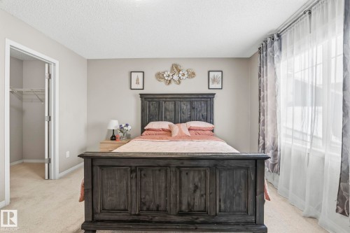 Bedroom featuring light-colored carpet, a large window with sheer and patterned curtains, and an open closet with wire shelving - 4783 Crabapplle Run, Edmonton, AB - Indoor Photo Showing Bedroom