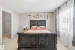 Bedroom featuring light-colored carpet, a large window with sheer and patterned curtains, and an open closet with wire shelving - 