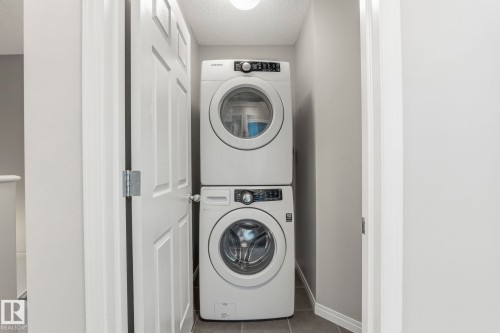 Dedicated laundry area featuring a white stackable washer and dryer unit, set against light gray walls with a matching baseboard, and dark gray tiled flooring - 4783 Crabapplle Run, Edmonton, AB - Indoor Photo Showing Laundry Room