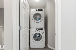 Dedicated laundry area featuring a white stackable washer and dryer unit, set against light gray walls with a matching baseboard, and dark gray tiled flooring - 