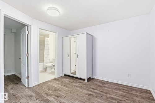 Room featuring wood-style flooring, light purple walls, a ceiling light fixture, and an open doorway leading to a bathroom with a white toilet and a shower with a patterned curtain - 4783 Crabapplle Run, Edmonton, AB - Indoor Photo Showing Other Room