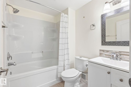 Bathroom featuring a white vanity with a rectangular sink, a patterned mirror, a white toilet, and a bathtub with an integrated shower - 4783 Crabapplle Run, Edmonton, AB - Indoor Photo Showing Bathroom