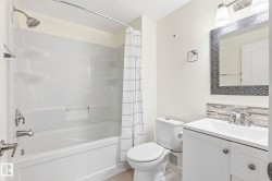 Bathroom featuring a white vanity with a rectangular sink, a patterned mirror, a white toilet, and a bathtub with an integrated shower - 