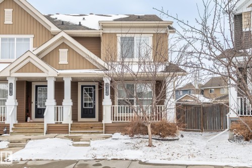 This property features a two-story exterior with a warm, neutral color palette, white trim, and a prominent front porch with white columns and railings - 4783 Crabapplle Run, Edmonton, AB - Outdoor With Facade