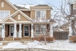 This property features a two-story exterior with a warm, neutral color palette, white trim, and a prominent front porch with white columns and railings - 