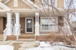 This property features a front porch with white columns and railings, a brown exterior with white trim, and a prominent front door with glass panels - 