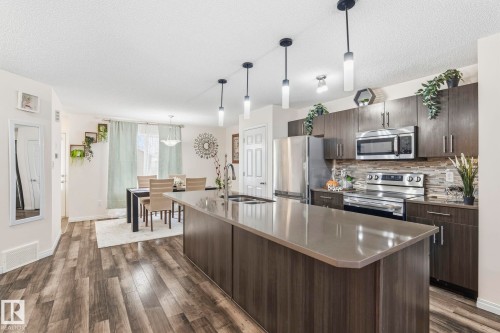The kitchen features stainless steel appliances, dark wood cabinetry, a tiled backsplash, and a large central island with a countertop - 4783 Crabapplle Run, Edmonton, AB - Indoor Photo Showing Kitchen With Upgraded Kitchen