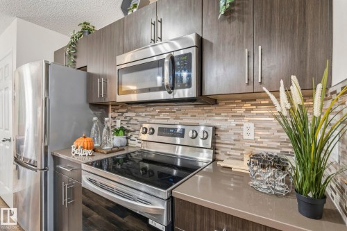 The kitchen features stainless steel appliances, dark wood-look cabinetry with silver hardware, a glass tile backsplash, and dark countertops - 4783 Crabapplle Run, Edmonton, AB - Indoor Photo Showing Kitchen