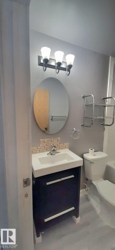 The bathroom features a vanity with a white sink, a modern dark cabinet with horizontal silver handles, and a tiled backsplash - 307 6307 118 Ave, Edmonton, AB - Indoor Photo Showing Bathroom