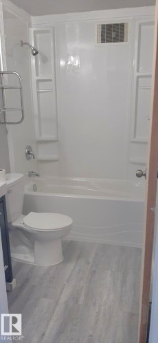 Bathroom featuring a white bathtub and shower combination, a white toilet, and light-colored wood-look flooring - 307 6307 118 Ave, Edmonton, AB - Indoor Photo Showing Bathroom
