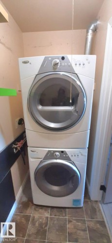 Laundry area featuring a stacked washer and dryer unit, tiled flooring, and light-colored walls - 307 6307 118 Ave, Edmonton, AB - Indoor Photo Showing Laundry Room