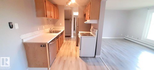 Kitchen featuring light wood cabinetry, a stainless steel sink, and a white electric range with an overhead hood - 307 6307 118 Ave, Edmonton, AB - Indoor