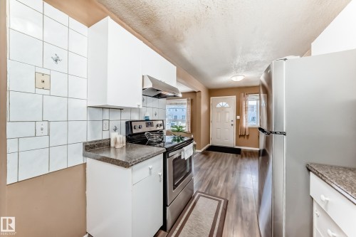 The kitchen features white cabinetry, a stainless steel oven with a range hood, and a stainless steel refrigerator - 6 1580 Millwoods Road E, Edmonton, AB - Indoor Photo Showing Kitchen With Upgraded Kitchen