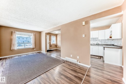 This inviting living area features warm-toned walls and wood-look flooring, extending into the entryway - 6 1580 Millwoods Road E, Edmonton, AB - Indoor