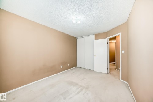 This room features light-colored carpeting, walls with a warm neutral tone, and a white ceiling with a textured finish - 6 1580 Millwoods Road E, Edmonton, AB - Indoor Photo Showing Other Room