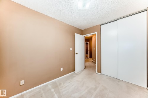 This room features neutral-toned walls, light-colored carpeting, a textured ceiling, and a large sliding door closet - 6 1580 Millwoods Road E, Edmonton, AB - Indoor Photo Showing Other Room