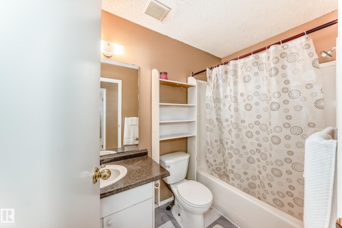 Bathroom featuring a vanity with an integrated sink and a dark countertop, a toilet, and a shower-tub combination - 6 1580 Millwoods Road E, Edmonton, AB - Indoor Photo Showing Bathroom