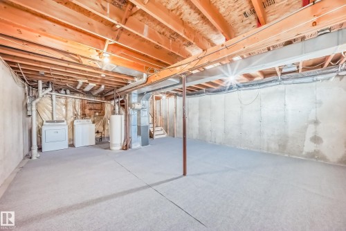 The unfinished basement includes exposed wooden beams, a water heater, and laundry appliances - 6 1580 Millwoods Road E, Edmonton, AB - Indoor Photo Showing Basement