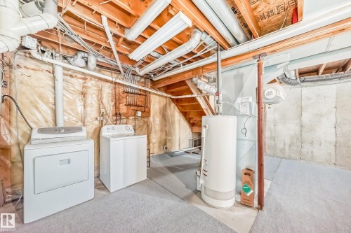The utility area includes a washer, dryer, and water heater, with exposed ceiling beams and concrete walls - 6 1580 Millwoods Road E, Edmonton, AB - Indoor