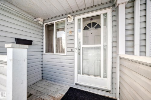 The property features a welcoming front entrance with light-colored siding, a window, and a white storm door with decorative glass - 6 1580 Millwoods Road E, Edmonton, AB - Outdoor With Exterior