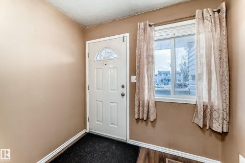 The property features a white paneled entry door with a decorative glass insert, accompanied by a window with blinds and patterned curtains - 6 1580 Millwoods Road E, Edmonton, AB - Indoor Photo Showing Other Room