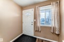 The property features a white paneled entry door with a decorative glass insert, accompanied by a window with blinds and patterned curtains - 6 1580 Millwoods Road E, Edmonton, AB  - Indoor Photo Showing Other Room 