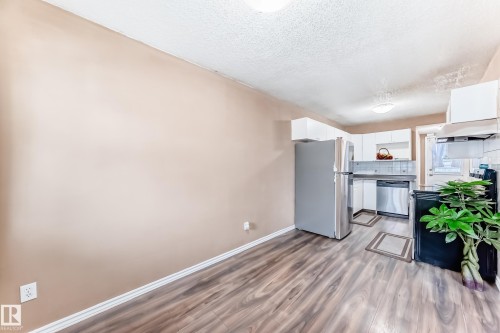 Kitchen area featuring wood-look flooring, white cabinetry, a stainless steel refrigerator, and a stainless steel dishwasher - 6 1580 Millwoods Road E, Edmonton, AB - Indoor