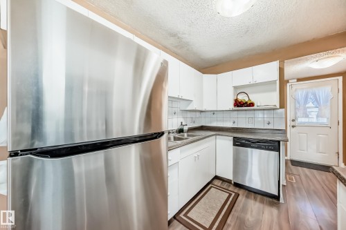 Well-appointed kitchen featuring a stainless steel refrigerator and dishwasher, white cabinetry, and a double sink - 6 1580 Millwoods Road E, Edmonton, AB - Indoor Photo Showing Kitchen With Double Sink