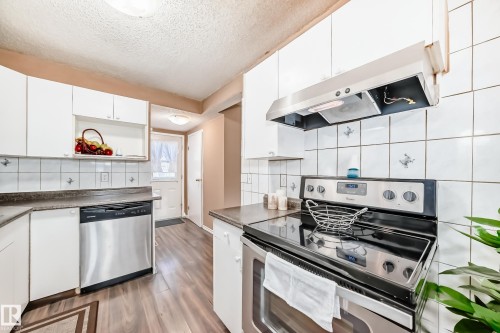 The kitchen features white cabinetry, white tile backsplash, stainless steel appliances, and wood-look flooring - 6 1580 Millwoods Road E, Edmonton, AB - Indoor Photo Showing Kitchen With Upgraded Kitchen