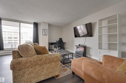 Living area featuring dark flooring, light-colored walls, and a large sliding glass door opening to a balcony - 1202 9909 110 Street Nw, Edmonton, AB - Indoor Photo Showing Living Room
