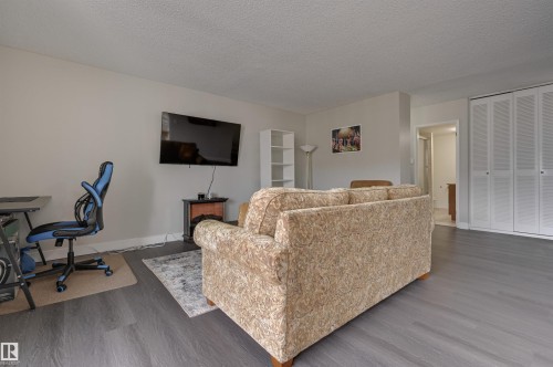 Living area featuring grey wood-style flooring, a wall-mounted television, and white bi-fold closet doors - 1202 9909 110 Street Nw, Edmonton, AB - Indoor Photo Showing Living Room